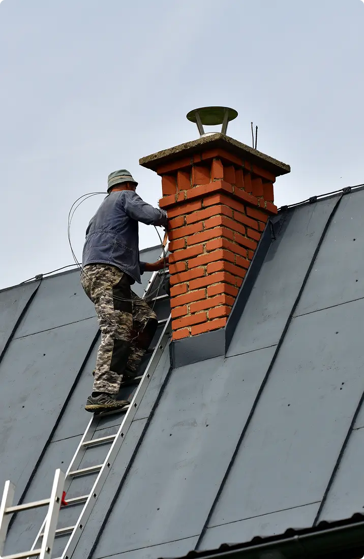 Worker repairing chimney on a rooftop ladder.